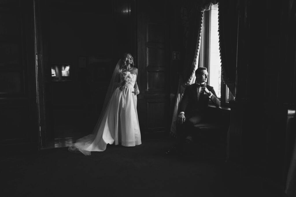 Para młoda w eleganckiej, czarno-białej aranżacji – panna młoda w sukni ślubnej i pan młody przy oknie – Karolina Koprowska Fotografia ślubna Łódź